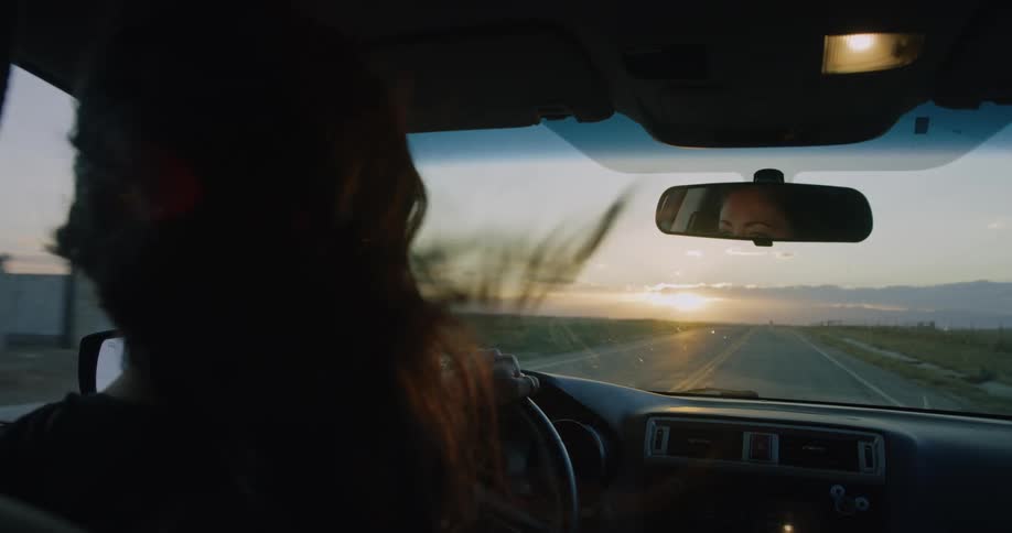 Woman driving a vehicle on a road with a sun on the horizon