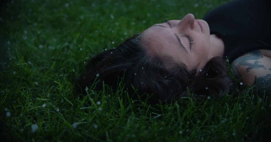 Woman lying on grass sleeping with snow falling
