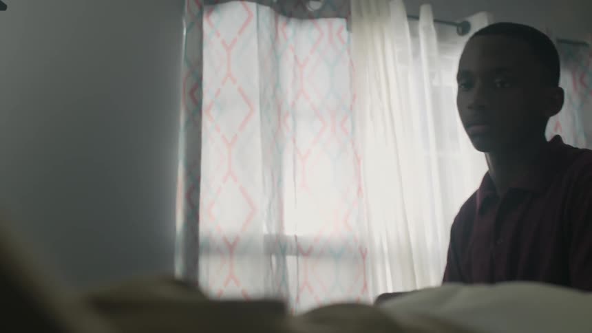 A boy walks up to a person in bed and sits down