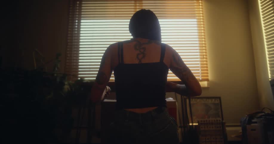 View of a woman from behind sitting in a room fixing her hair and taking an object from a box