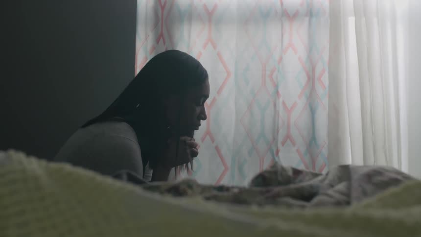 A woman sits thinking next to a bedroom window