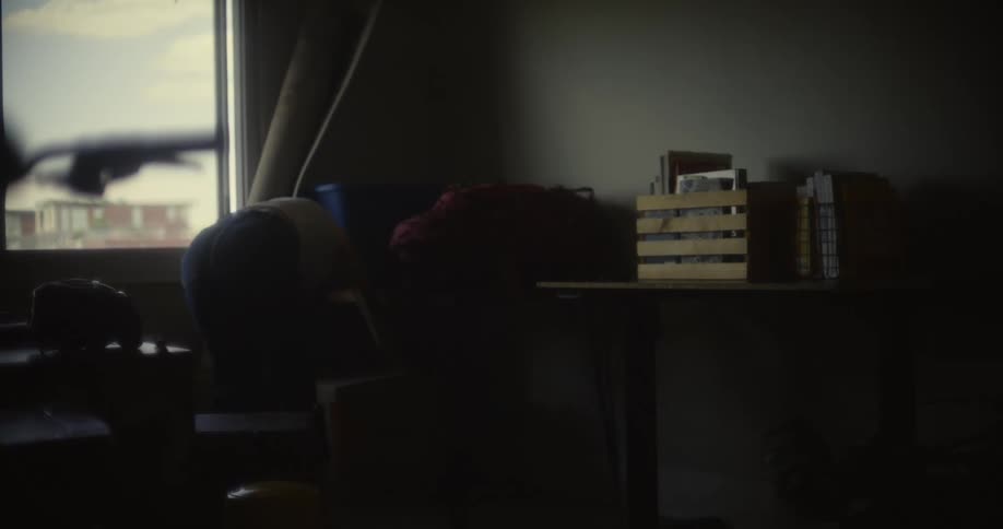 A woman in a dimly lit room picks up a cardboard box and walks out