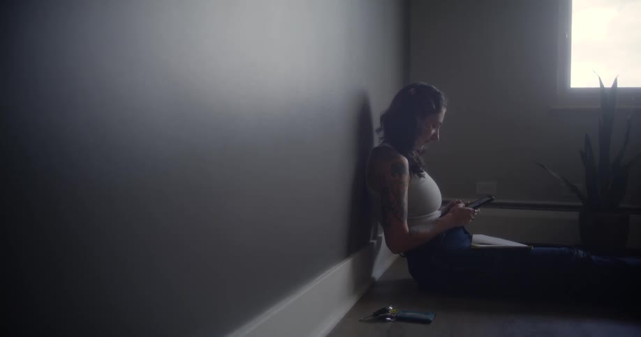 Woman sitting on the floor next to potted plants in a bedroom and typing on a smartphone