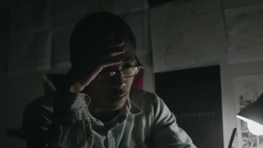 Spectacled man sitting at a desk pondering something while he taps his pen on the table