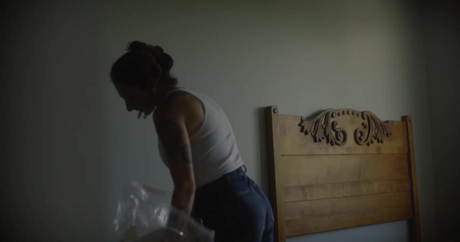 A woman makes the bed in her bedroom next to a window with sunlight streaming in