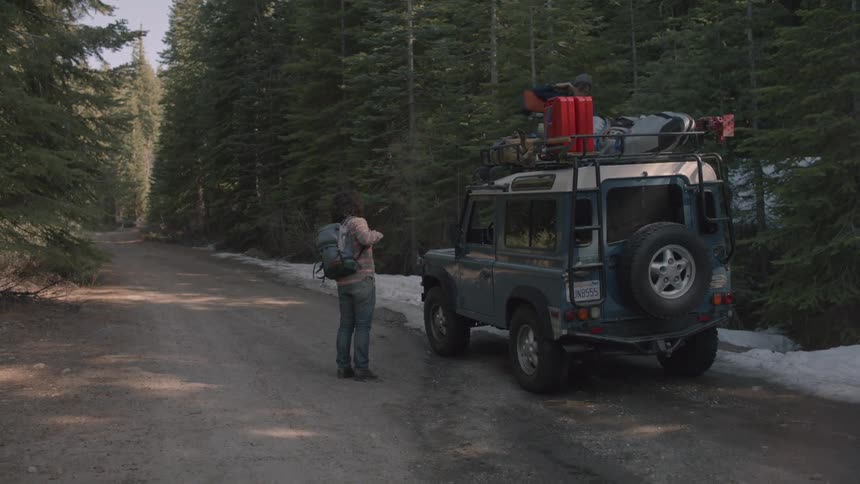 Man on top of vehicle throws bag down and then they walk down a road