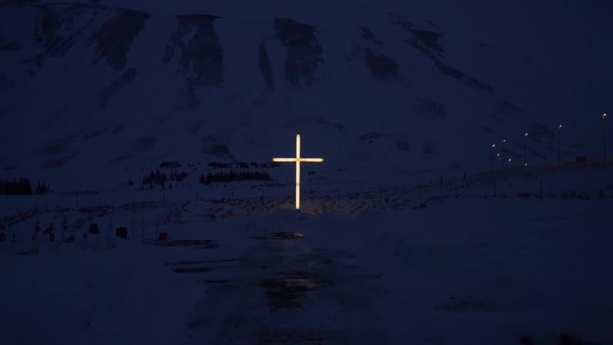 Glowing cross on snow covered ground with a mountain in the background at night