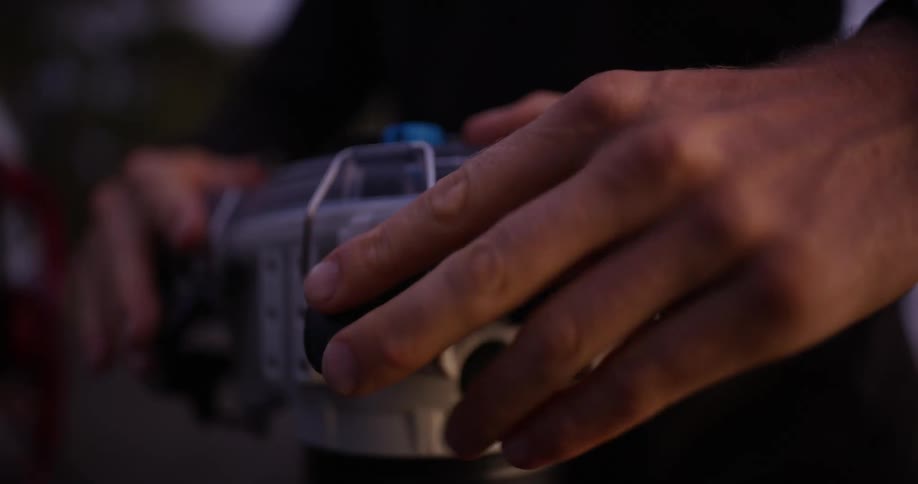 A person adjusts or operates a white and black camera or filming device with a rotating barrel likely for professional filming purposes