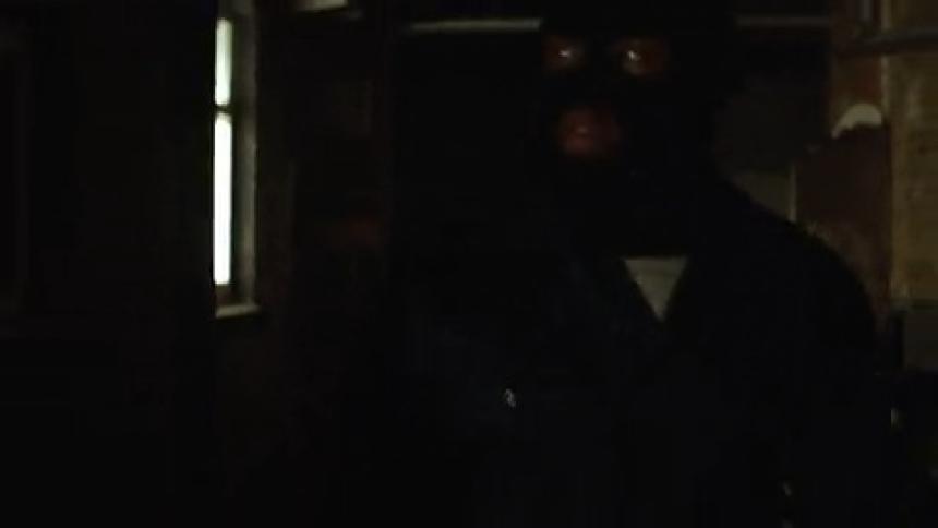 A thief in a mask exits an industrial warehouse