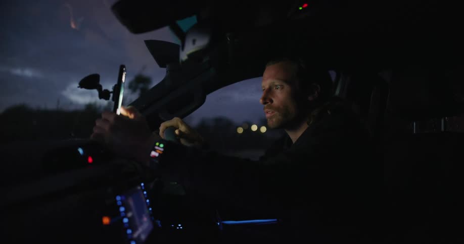 Man sitting in a vehicle at night checks the navigation app on his smartphone