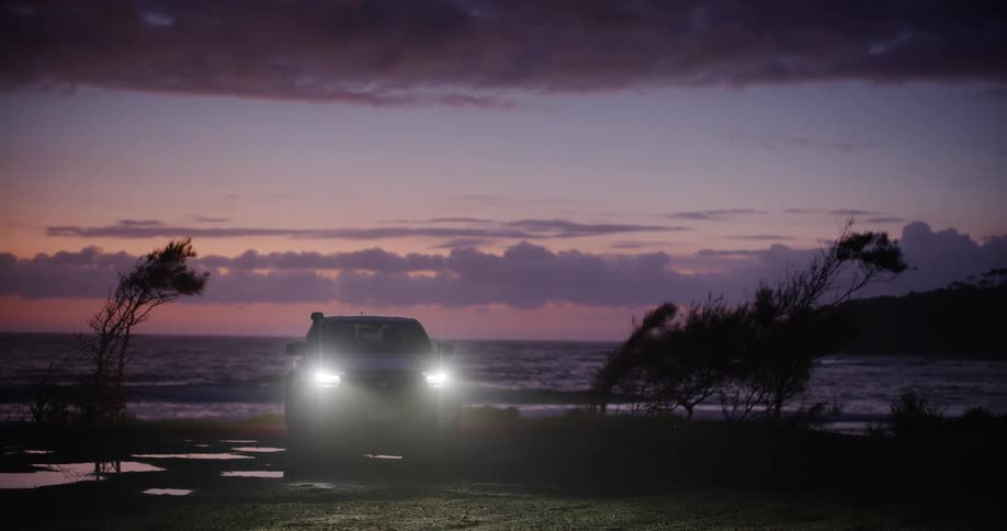 Truck on the beach backs up to the surf under a red tinted sky