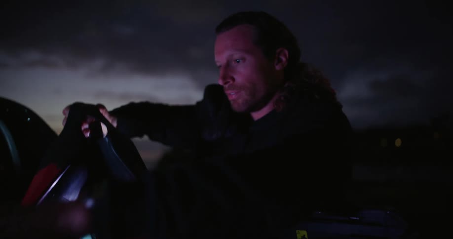 Man riding in the back of a pickup truck and picking up equipment while the car is parked in a natural area at dark dawn