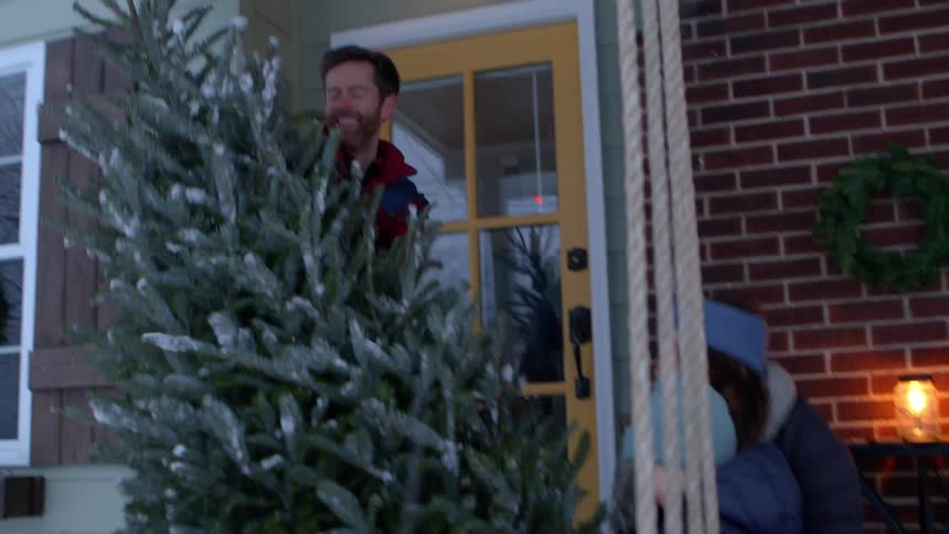 A father carries a christmas tree to the home as it snows