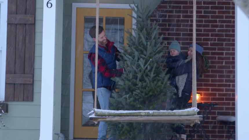 Family in the backyard of a house with a christmas tree on a snowy day