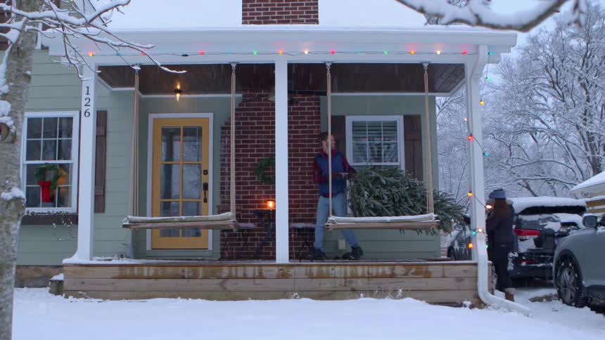 A family brings their christmas tree to the porch of their snow covered house