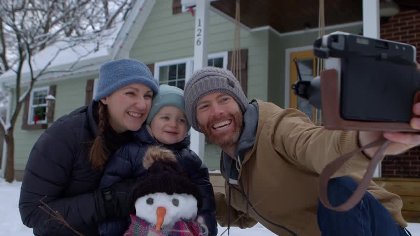 Family takes a picture of themselves posing with a small snowman in their front yard on a winter day