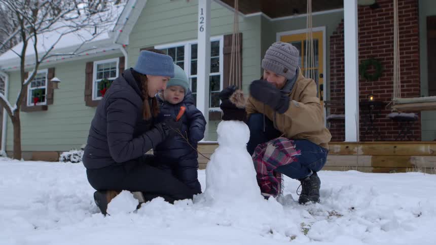 Father and mother with their son next to a snowman in the backyard