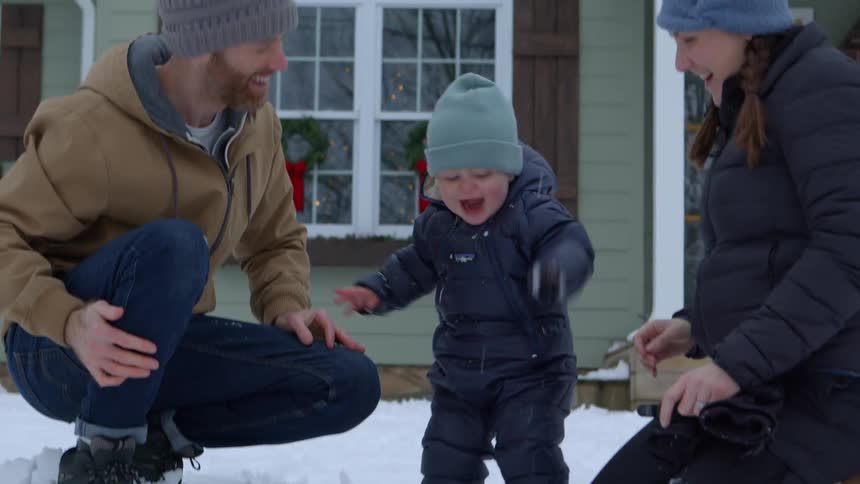 Parents show their child how to play in the snow while in their front yard
