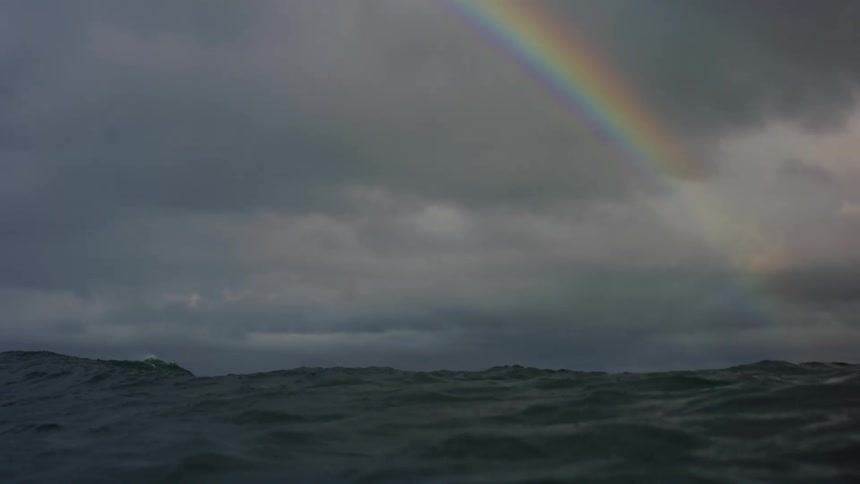 High waves in the ocean below a rainbow in a stormy sky