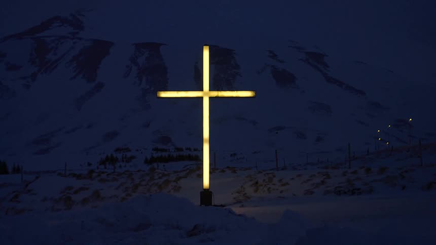A cross of neon lights glows yellow in total darkness