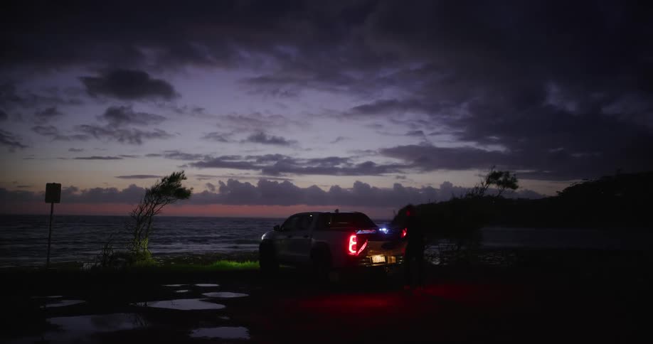 Man opens the tailgate of a pickup parked on the coast in the evening