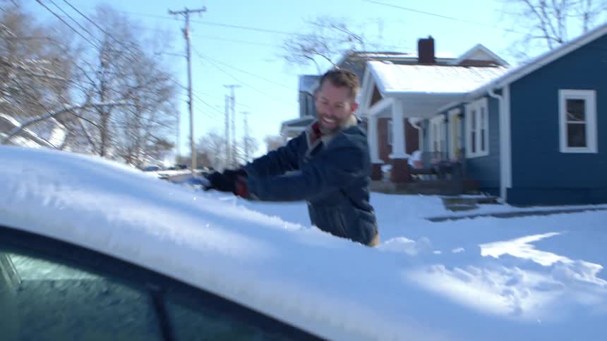 Man in a denim jacket brushing off snow from car window