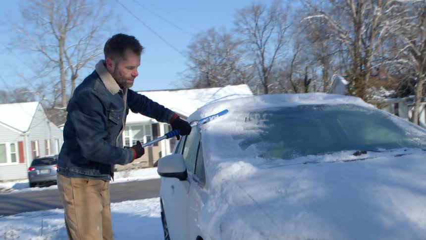 Man removing snow from the front of his car