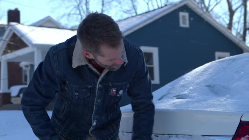 Man with a broom removing snow from a car
