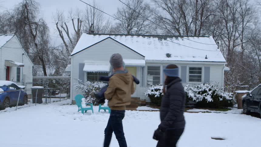 Family with a small child walking in the snow next to a house in an urban neighborhood