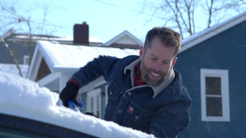Man smiles while scraping ice off his car parked at home on a winter day