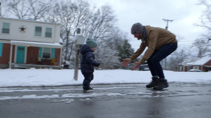On a snowy day a toddler walks toward their dad and is picked up