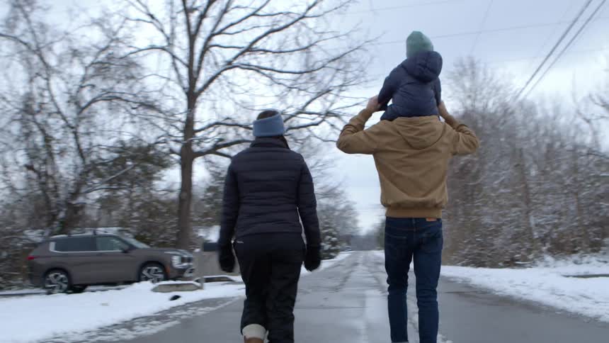 Family of three walking down a snowy neighborhood street with the toddler on the fathers shoulders