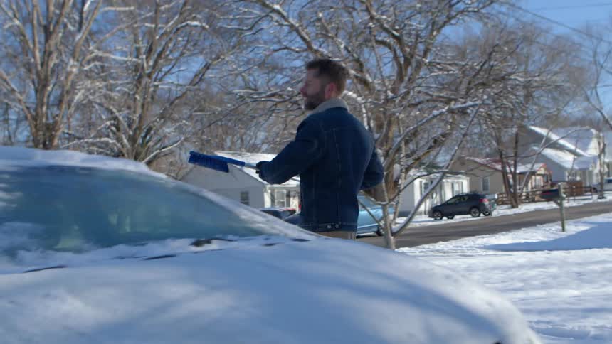 A man using a shovel to clear snow from the windshield of a car
