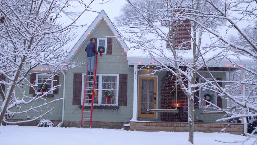 Man installing a wreath on the upper window of a townhouse on a snowy day