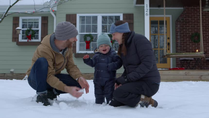 A family is playing in the snow in front of a house decorated with holiday wreaths and lights