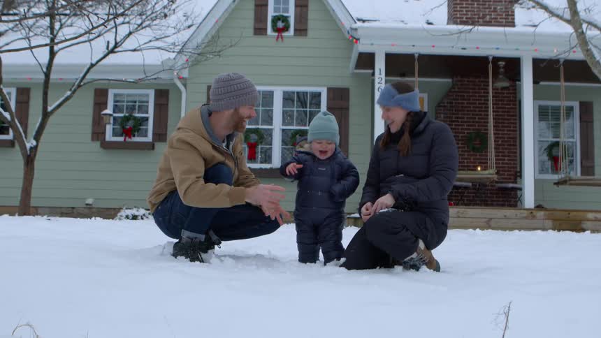 Father and mother in the backyard playing with their little son in the snow