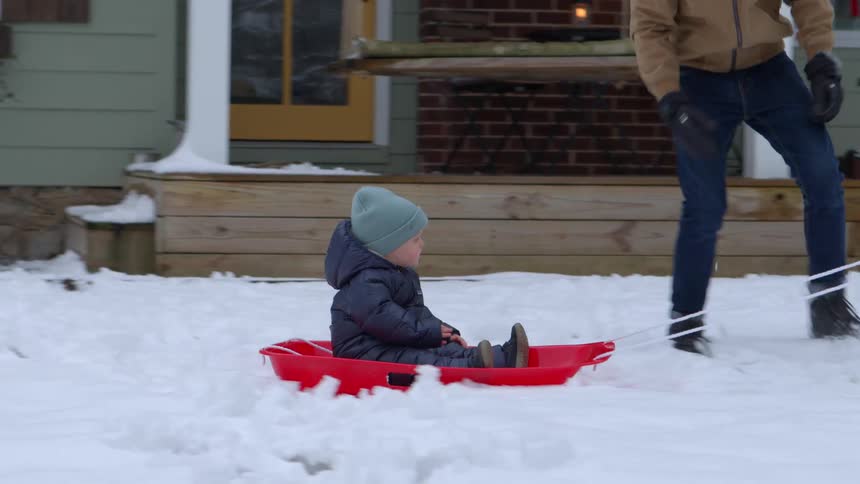 Mom pulling baby in a sled on front lawn as dad runs alongside him