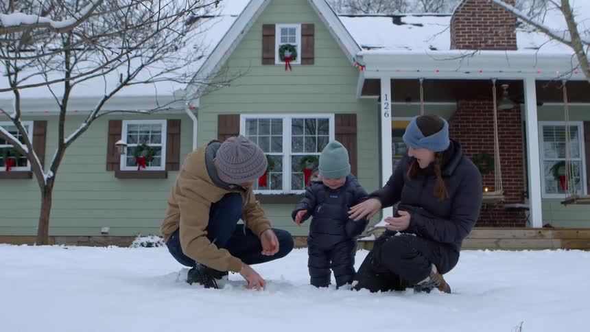 Young family with a baby playing in the snow on the front lawn