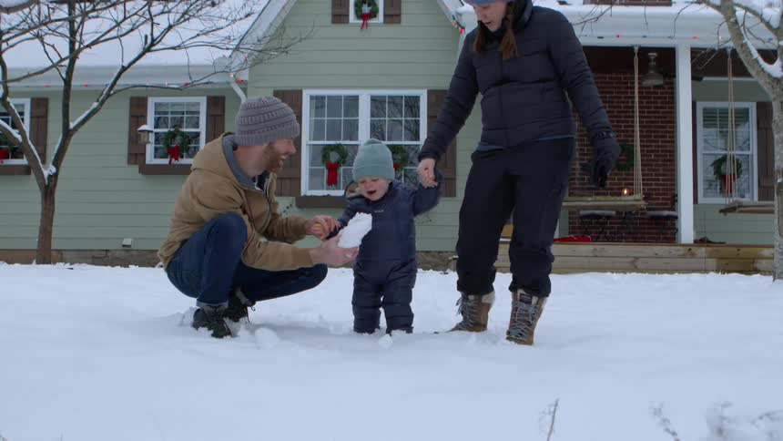 Parents take their toddler outdoors to interact with the snow on a winter day