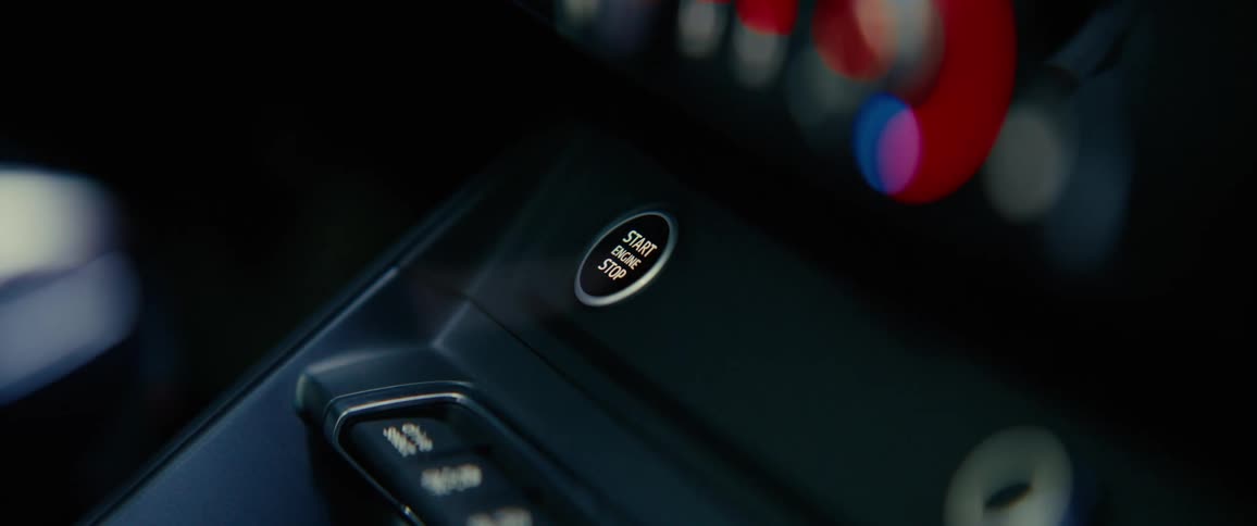 A finger presses the start button on a dark dashboard of a car