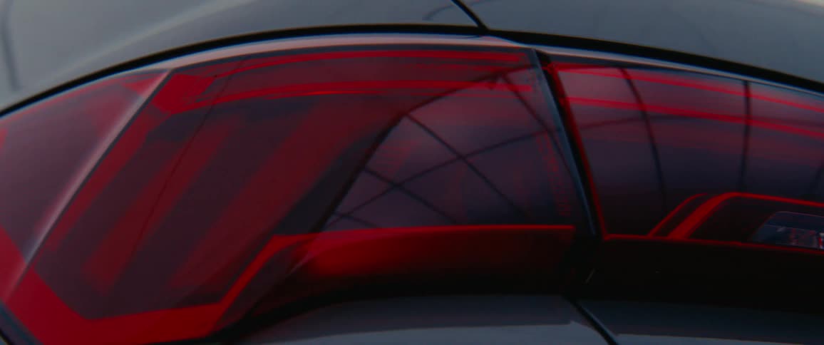 A closeup of a cars taillight shows a glowing red light with intricate internal patterns