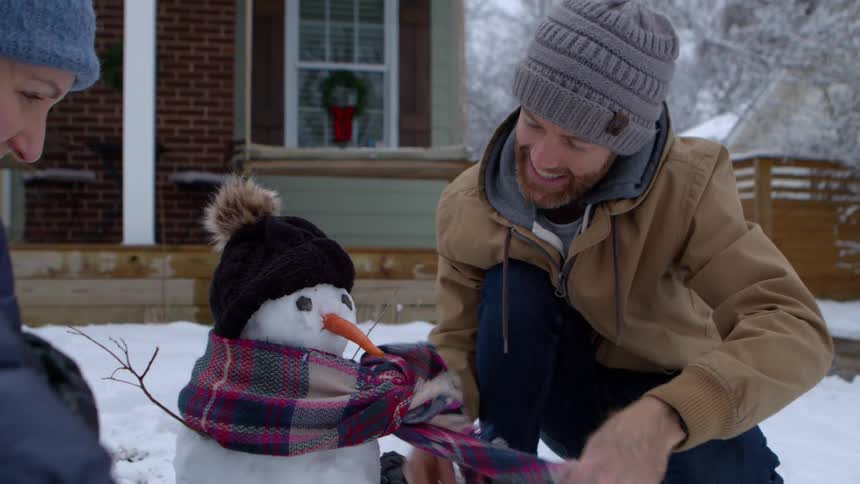 Couple in backyard putting a scarf on a snowman