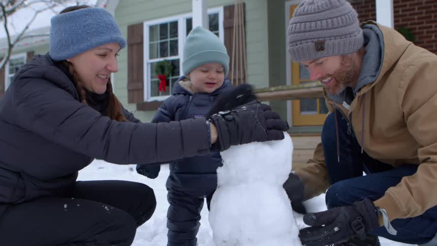 A family builds a snowman in front of their home during the christmas season