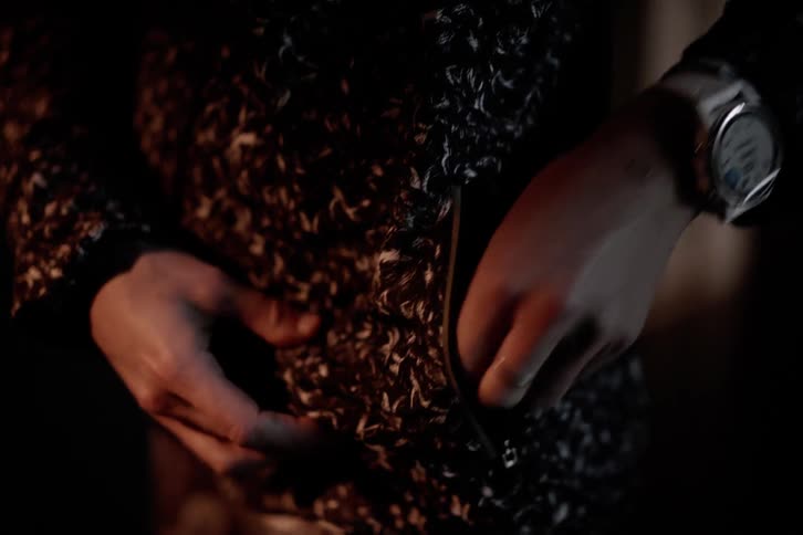 Woman standing indoors unzips her pocket to extract a filled tube container