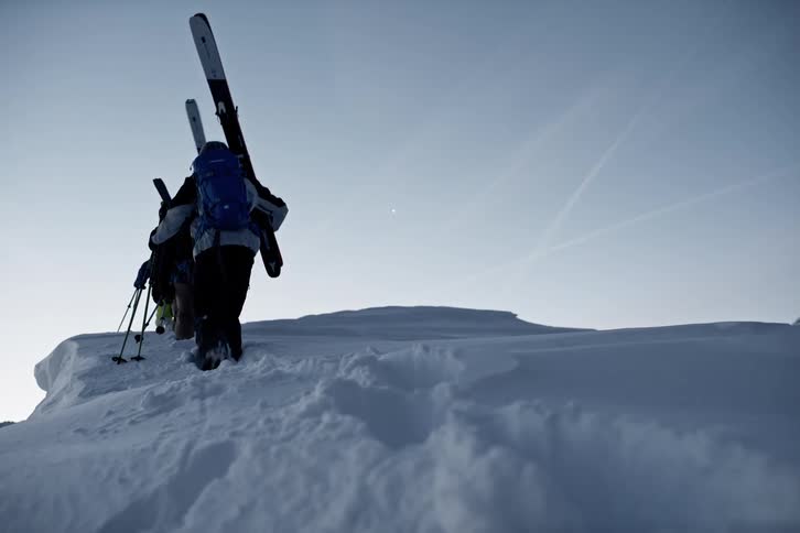 Group of skiers hiking up summit of snow covered mountain peak