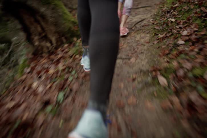 Closeup of two peoples feet running down a trail