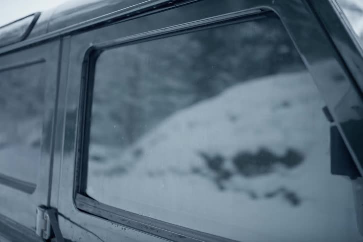 Vehicles side window its tinted glass reflecting a blurry snow covered scene