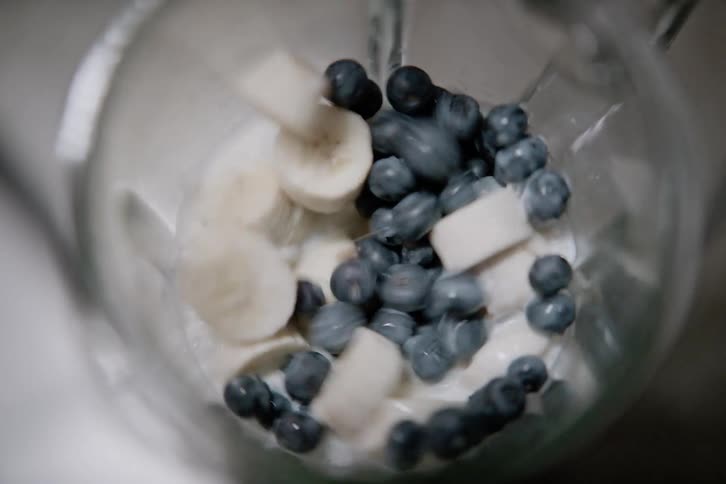 Blueberries and banana slices are inside a blender being blended into a smoothie