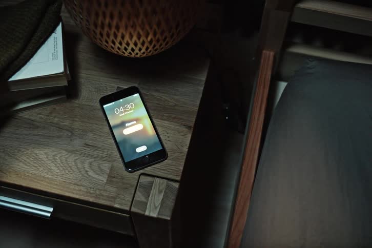 A cell phone on a wooden table and then the screen turns on and a persons hand picks it up