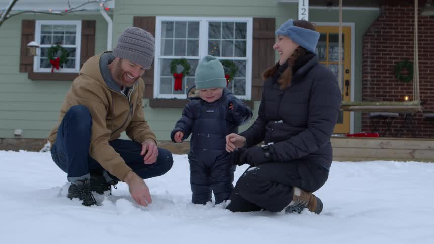 A family is playing in the snow in front of a house decorated with holiday wreaths and lights